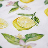 A close-up of a white fabric with a watercolor-style print of lemons, green leaves, and small pink flowers.