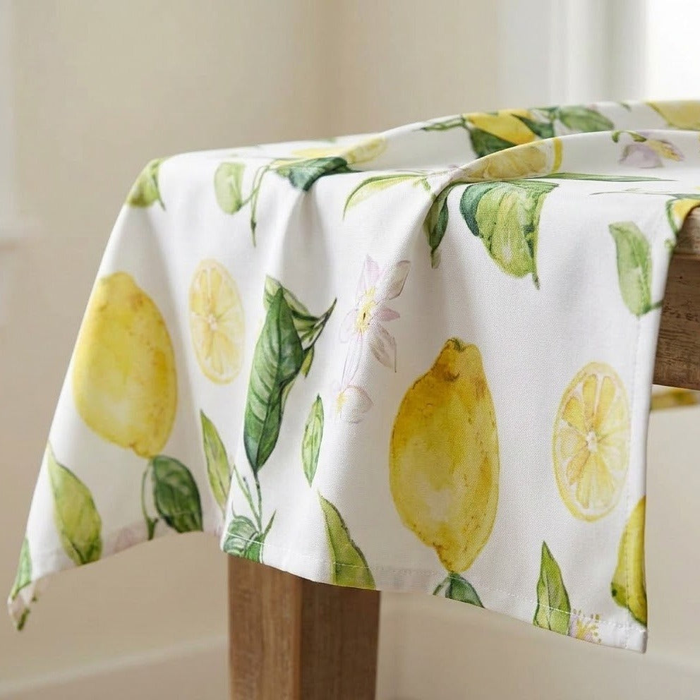 A white tablecloth with a watercolor-style lemon and leaf pattern draped over a wooden table in a softly lit indoor setting.