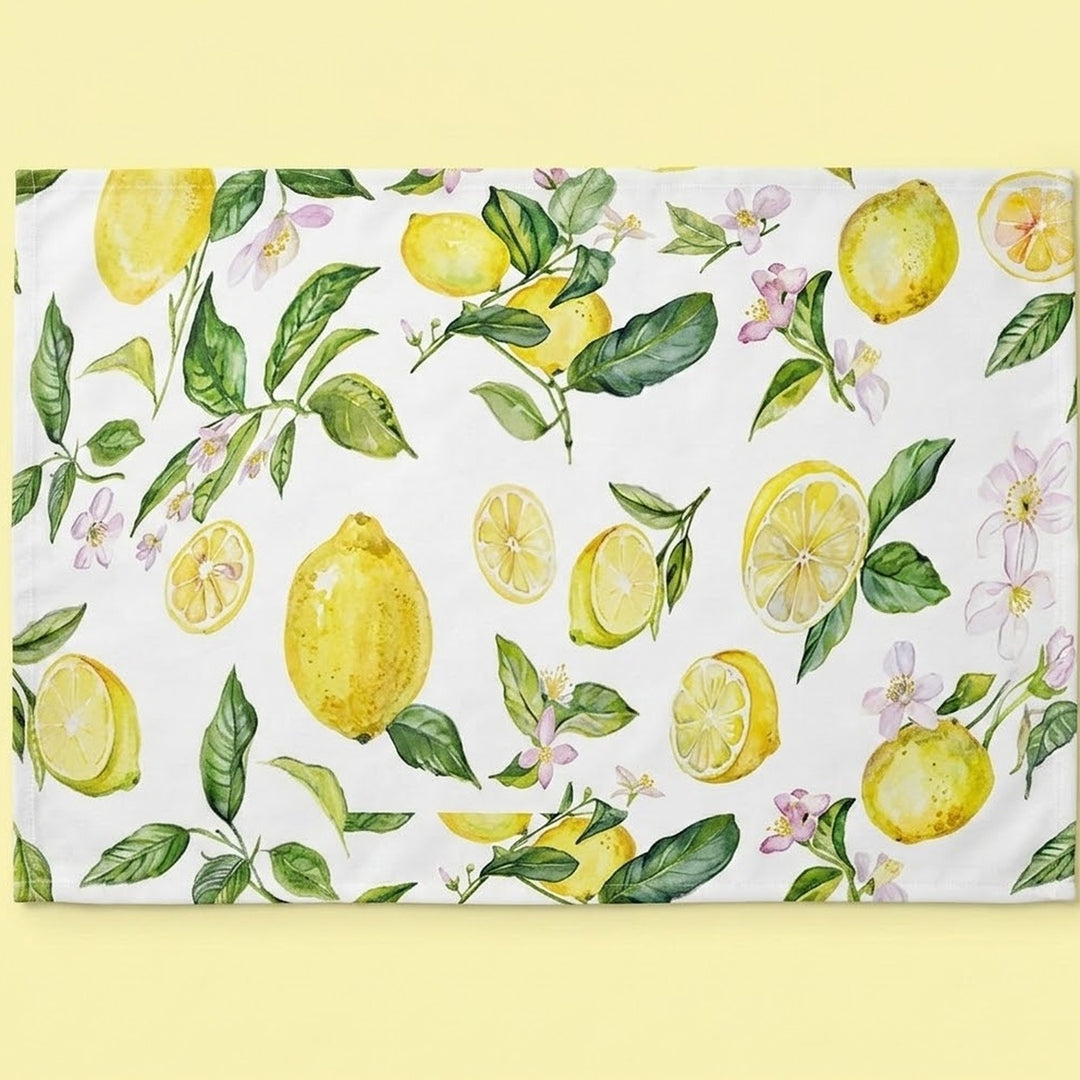 A rectangular white kitchen towel or placemat featuring a watercolor-style lemon and leaf pattern, displayed flat against a pale yellow background.