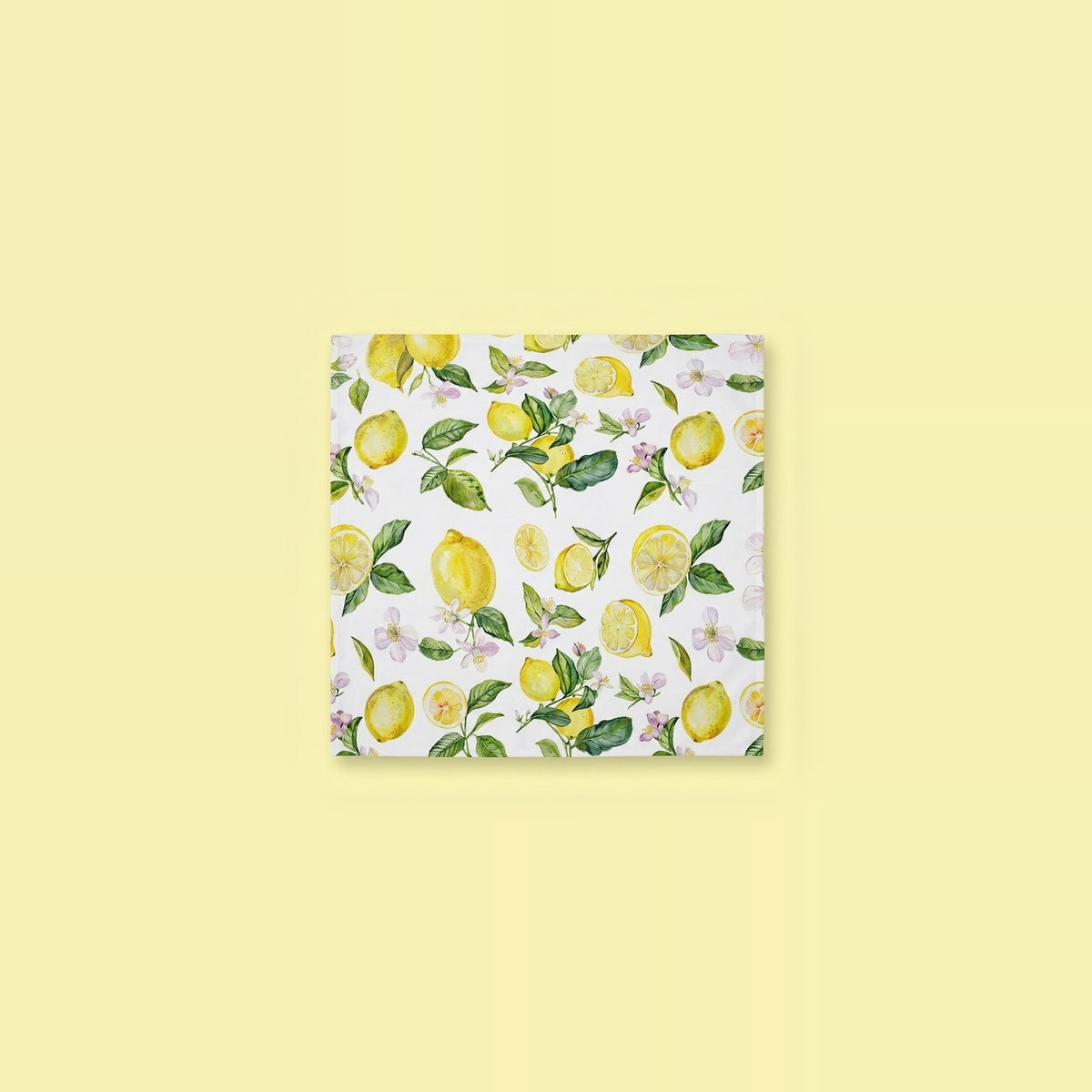 A square white napkin featuring a watercolor-style lemon and leaf pattern, centered on a pale yellow background.