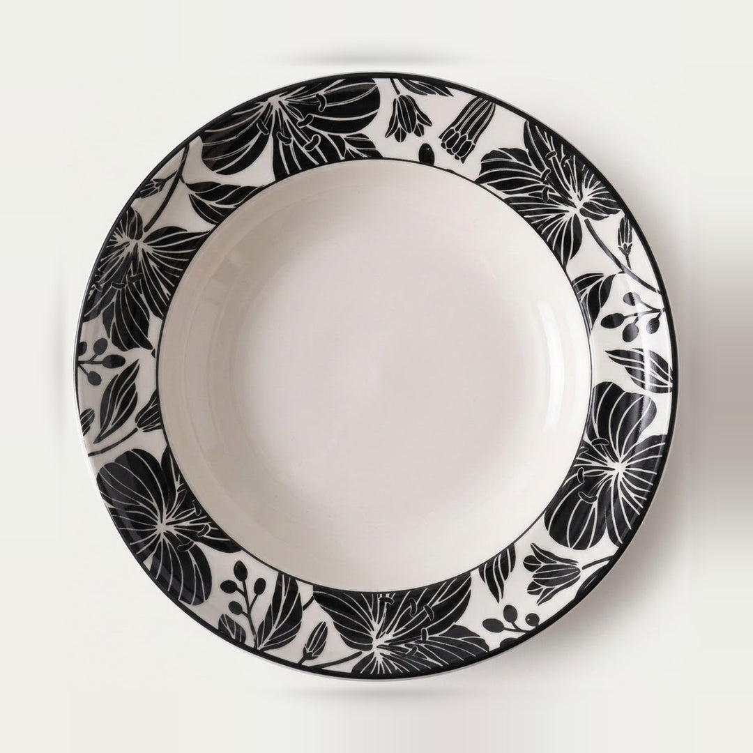 A round white ceramic plate with a wide black floral border pattern, photographed from directly above on a clean white background.
