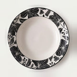A round white ceramic plate with a wide black floral border pattern, photographed from directly above on a clean white background.