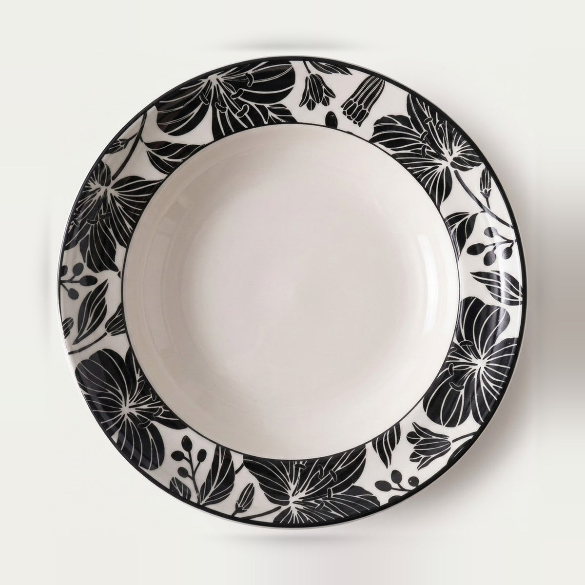 A round white ceramic plate with a wide black floral border pattern, photographed from directly above on a clean white background.