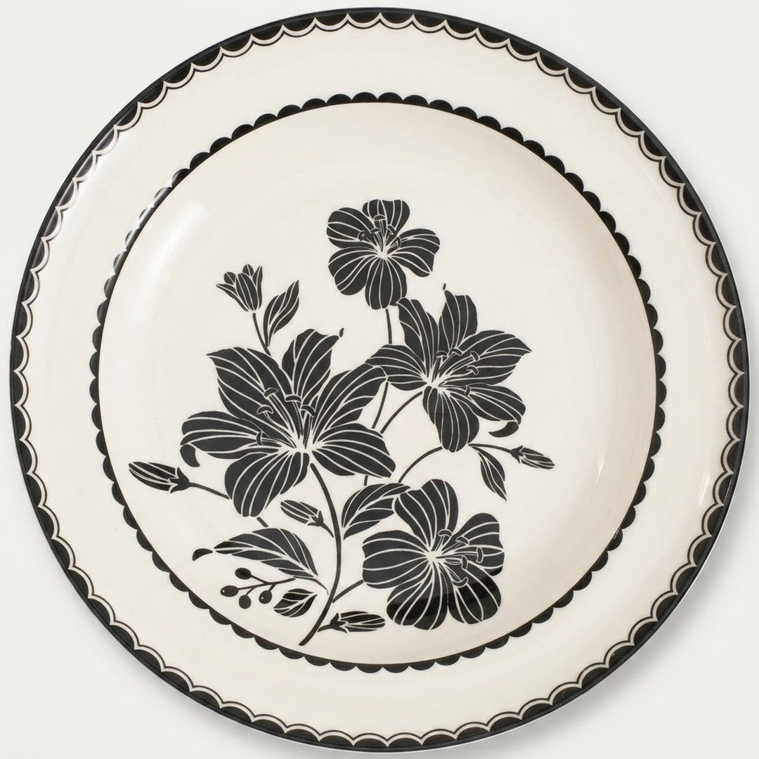 An off-white ceramic plate featuring a black floral design in the center and a black scalloped rim, shown against a plain light background.