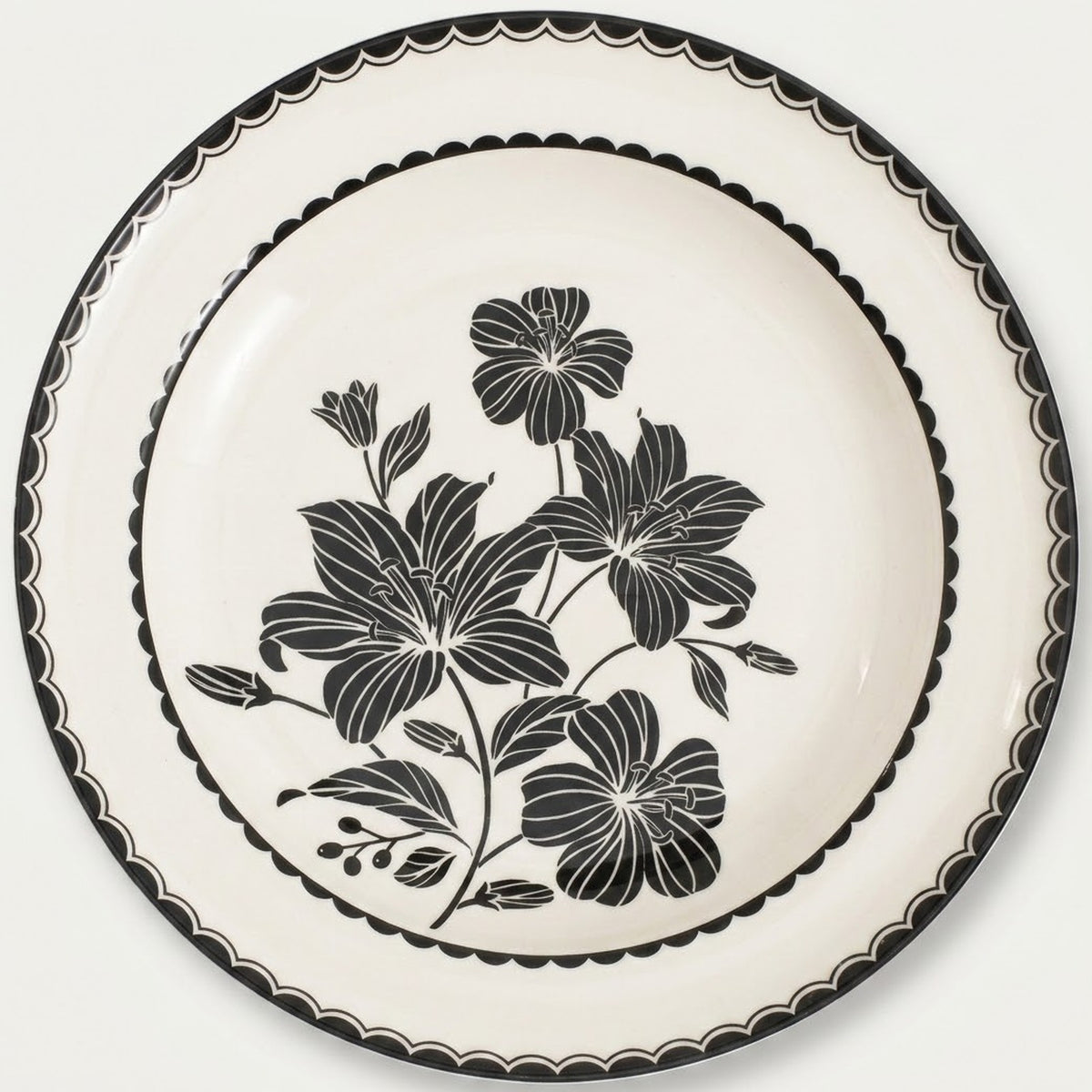 An off-white ceramic plate featuring a black floral design in the center and a black scalloped rim, shown against a plain light background.
