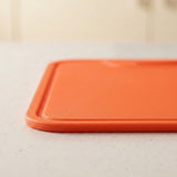 An orange silicone cutting board lid or cover resting on a light speckled countertop.