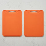 Two bright orange rectangular cutting boards with integrated handle cutouts, shown side by side on a light gray marble-textured surface.
