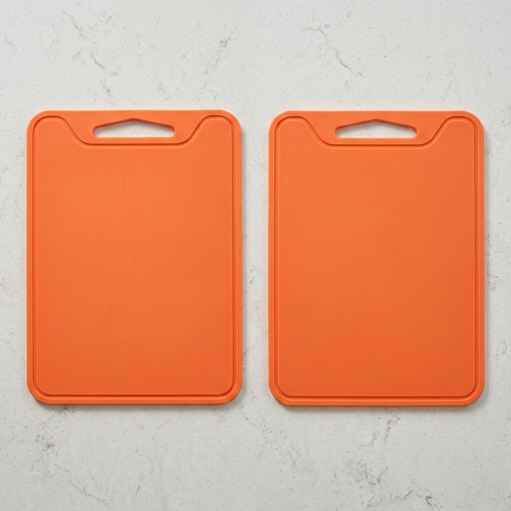 Two bright orange rectangular cutting boards with integrated handle cutouts, shown side by side on a light gray marble-textured surface.