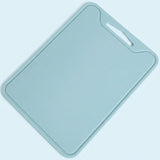 A light blue rectangular cutting board with rounded corners and a built-in handle cutout in the top right corner, shown on a matching light blue background.