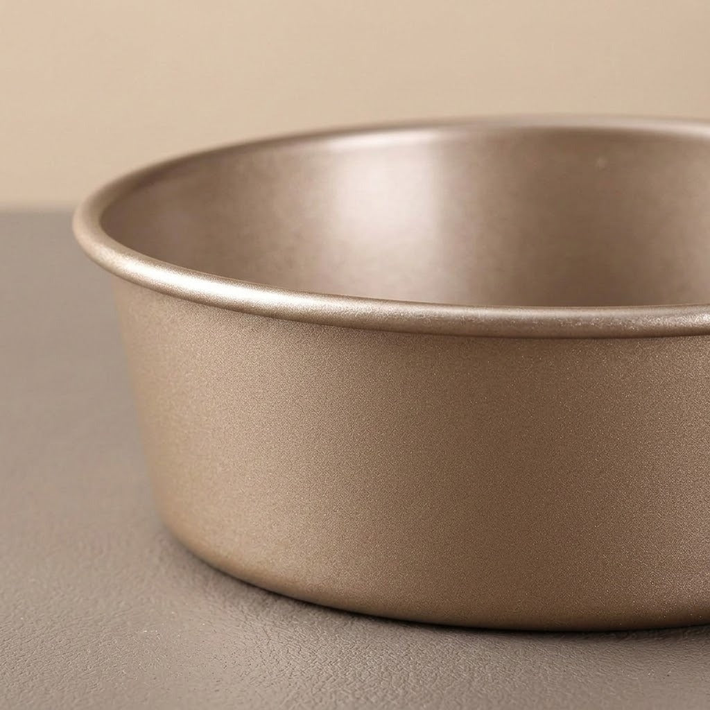 A close-up of a round metal cake pan with a matte metallic finish, set against a neutral beige background.