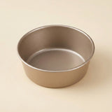 A round metal cake pan with a non-stick coating, shown from a top-down perspective on a light beige background.