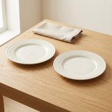 An off-white ceramic cup with embossed floral patterns sits on a light wood table next to a beige cloth napkin and a silver spoon.