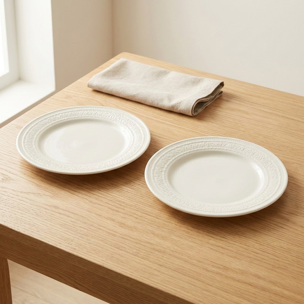 An off-white ceramic cup with embossed floral patterns sits on a light wood table next to a beige cloth napkin and a silver spoon.