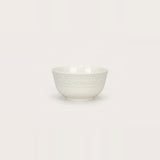 A small white ceramic bowl with a textured, embossed floral pattern around the upper half, shown against a solid, warm off-white background.