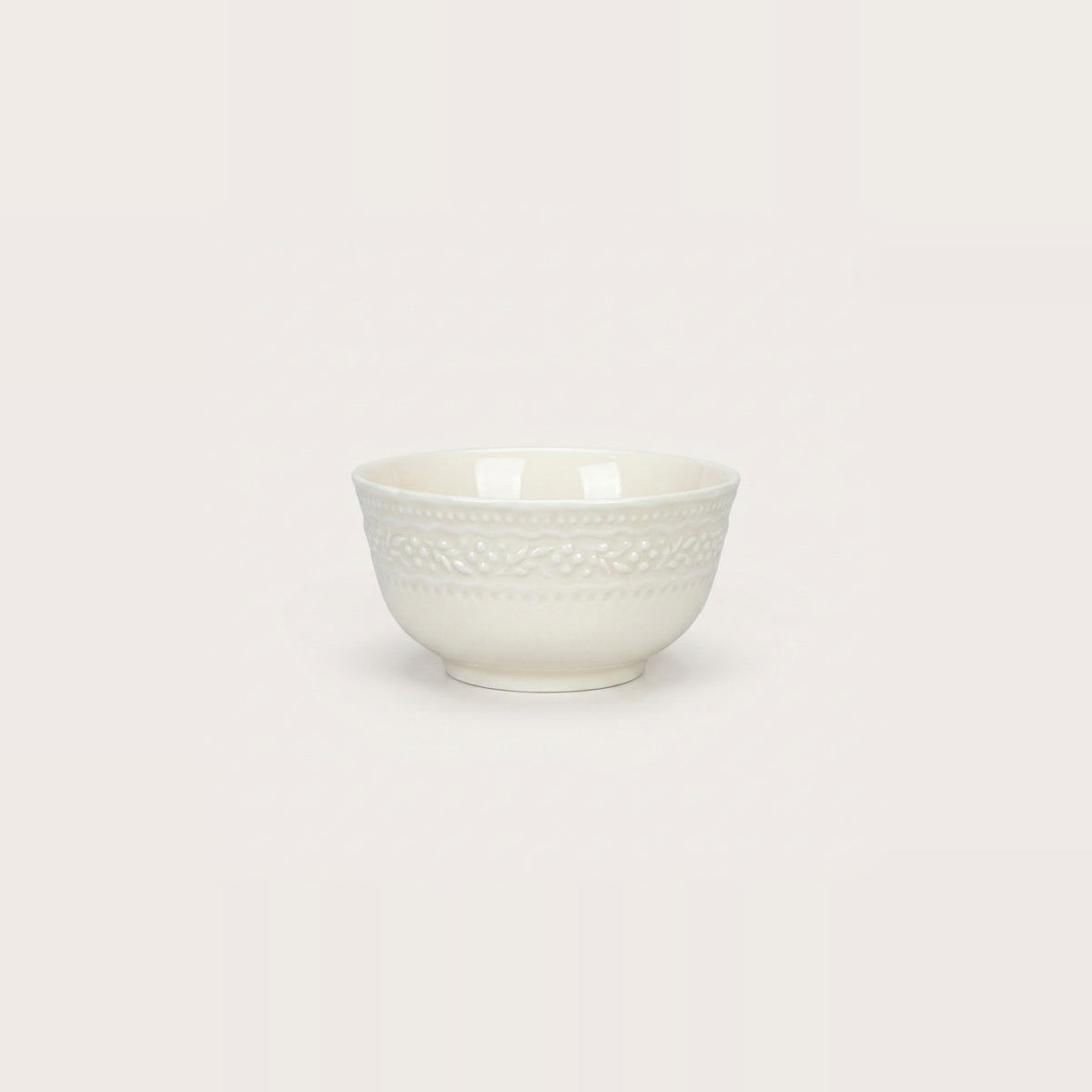 A small white ceramic bowl with a textured, embossed floral pattern around the upper half, shown against a solid, warm off-white background.