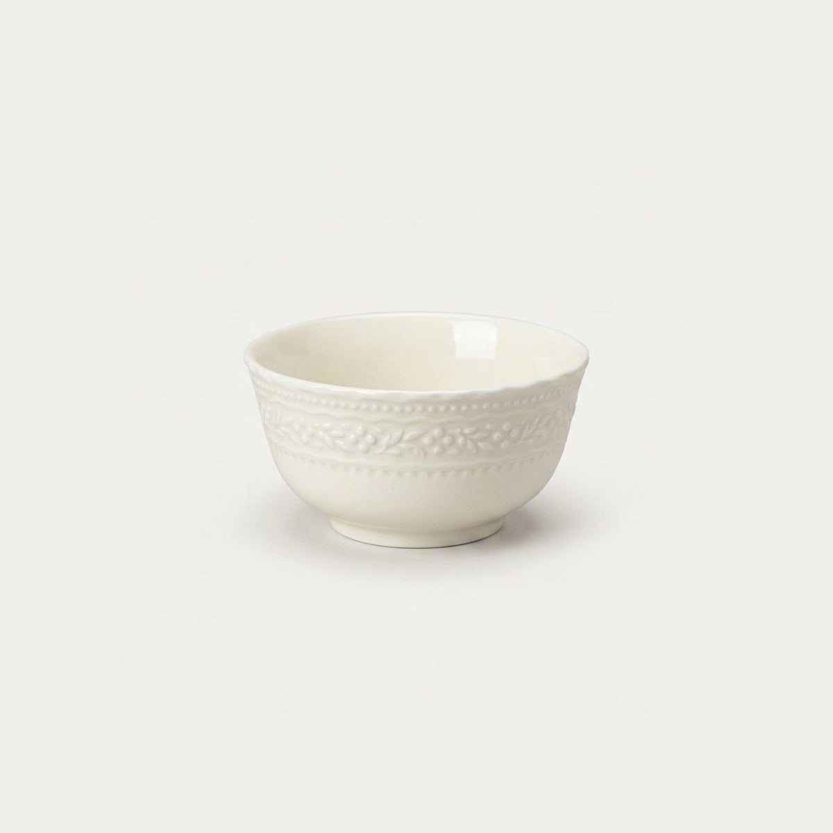 A small off-white ceramic bowl with a textured beaded border pattern, photographed against a seamless light gray background.