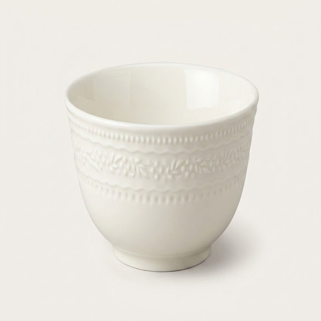 A white ceramic cup with a textured, embossed floral band around the middle, shown on a clean, light beige background.