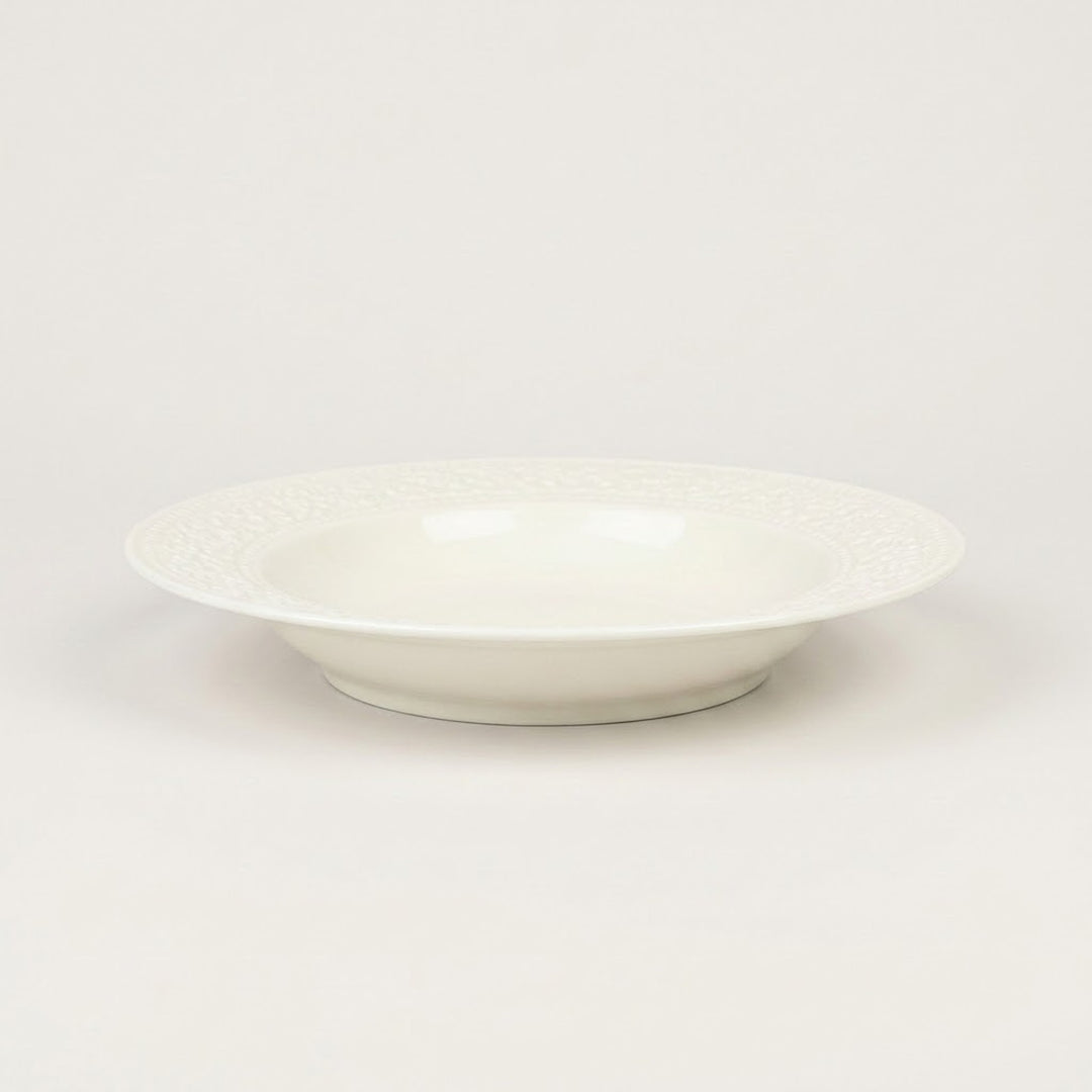 A white ceramic bowl with a subtle textured pattern on the outer rim, photographed against a seamless light gray background.
