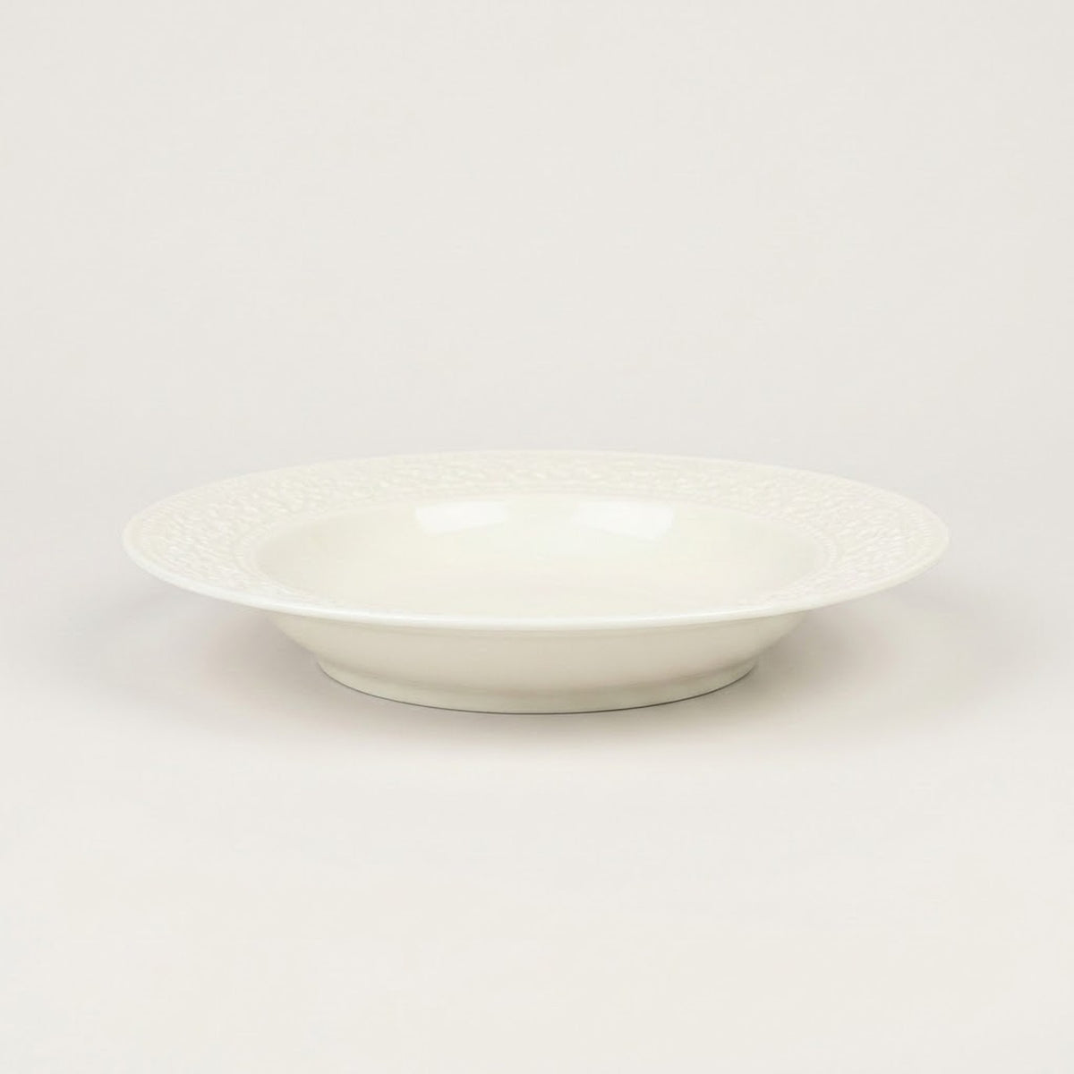 A white ceramic bowl with a subtle textured pattern on the outer rim, photographed against a seamless light gray background.