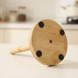 A bamboo kitchen tool with a round light wood head, four black rubber feet, and a light bamboo handle, resting on a white kitchen counter.