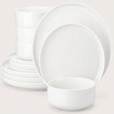 A white ceramic dinnerware set including plates and bowls, arranged on a light beige background.