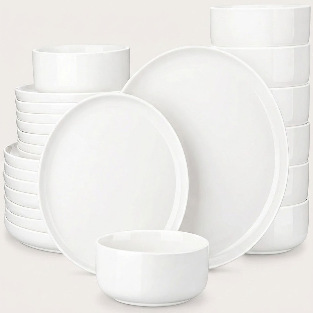 A set of white ceramic dinnerware, including plates and bowls, arranged on a light beige background.