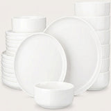 A set of white ceramic dinnerware, including plates and bowls, arranged on a light beige background.