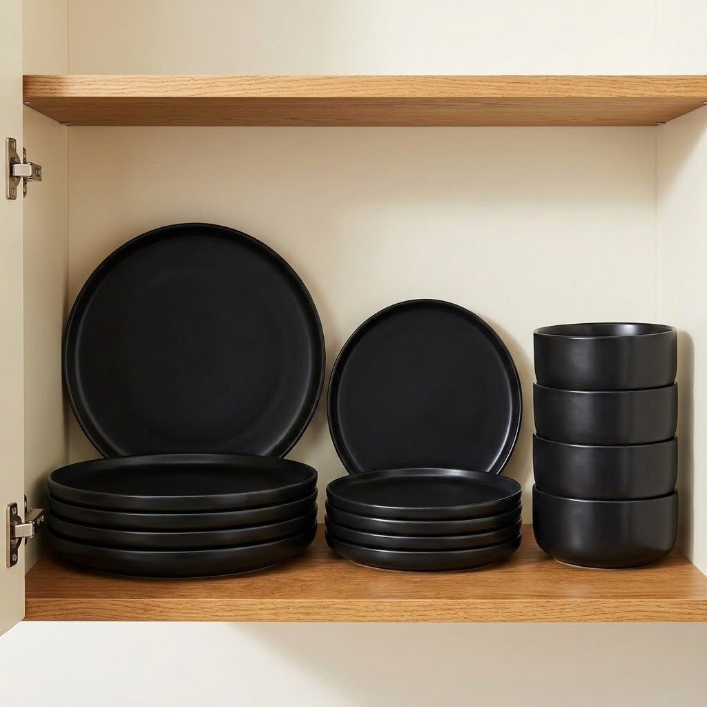 A set of matte black dinnerware, including plates and bowls, neatly arranged inside a wooden cabinet with a cream-colored lining.