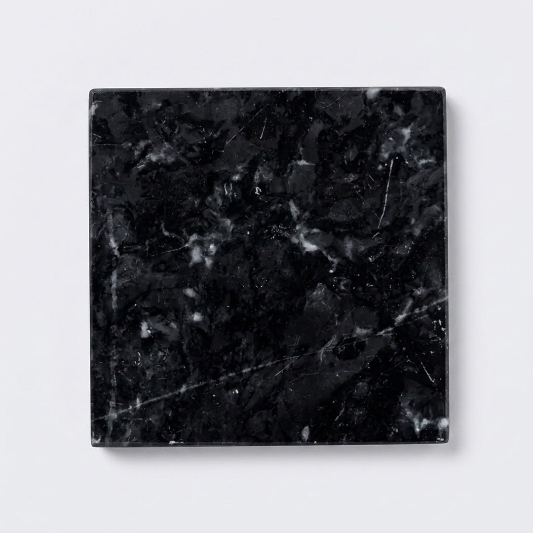 A square black marble tile coaster with white and gray veining, shown from a top-down perspective on a light gray background.