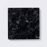 A square black marble tile coaster with white and gray veining, shown from a top-down perspective on a light gray background.