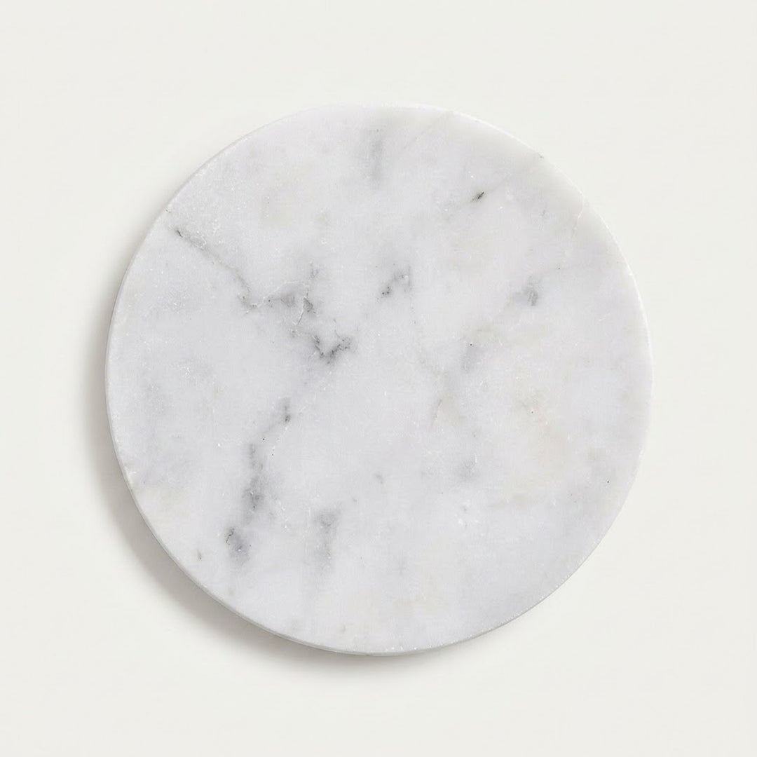 A round white marble coaster with natural gray and black veining, shown on a clean off-white background.