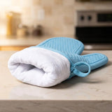 A light blue and white oven mitt resting on a beige marble countertop with a blurred kitchen background.