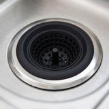 A close-up of a kitchen sink drain insert with a black perforated center and a brushed silver metal rim set into a stainless steel sink.