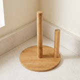 A light natural bamboo table stand with a round base, one upright post, and one shorter side post, placed on a light stone countertop in a kitchen corner.