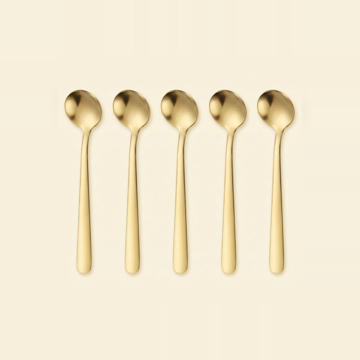 Five gold-colored metal spoons arranged in a row against a solid cream-colored background.