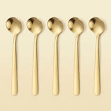Five gold-toned metal spoons arranged in a row on a light beige background.