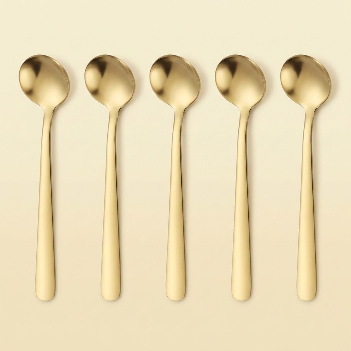 Five gold-toned metal spoons arranged in a row on a light beige background.