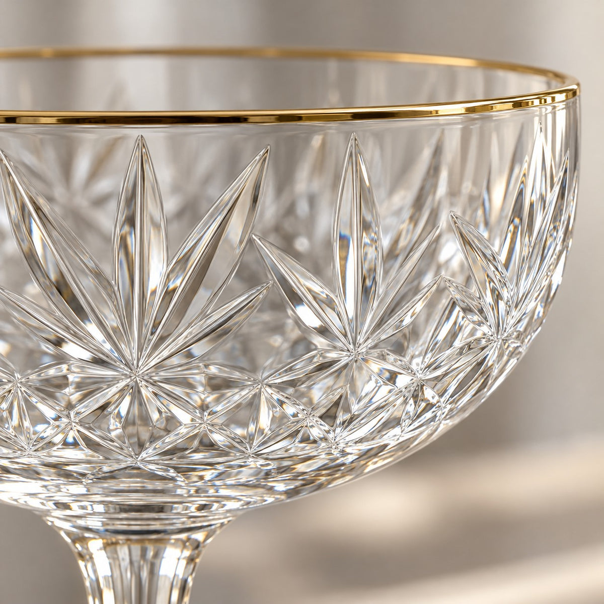 A macro view shows the coupe glass's clear engraved facets and polished gold rim.