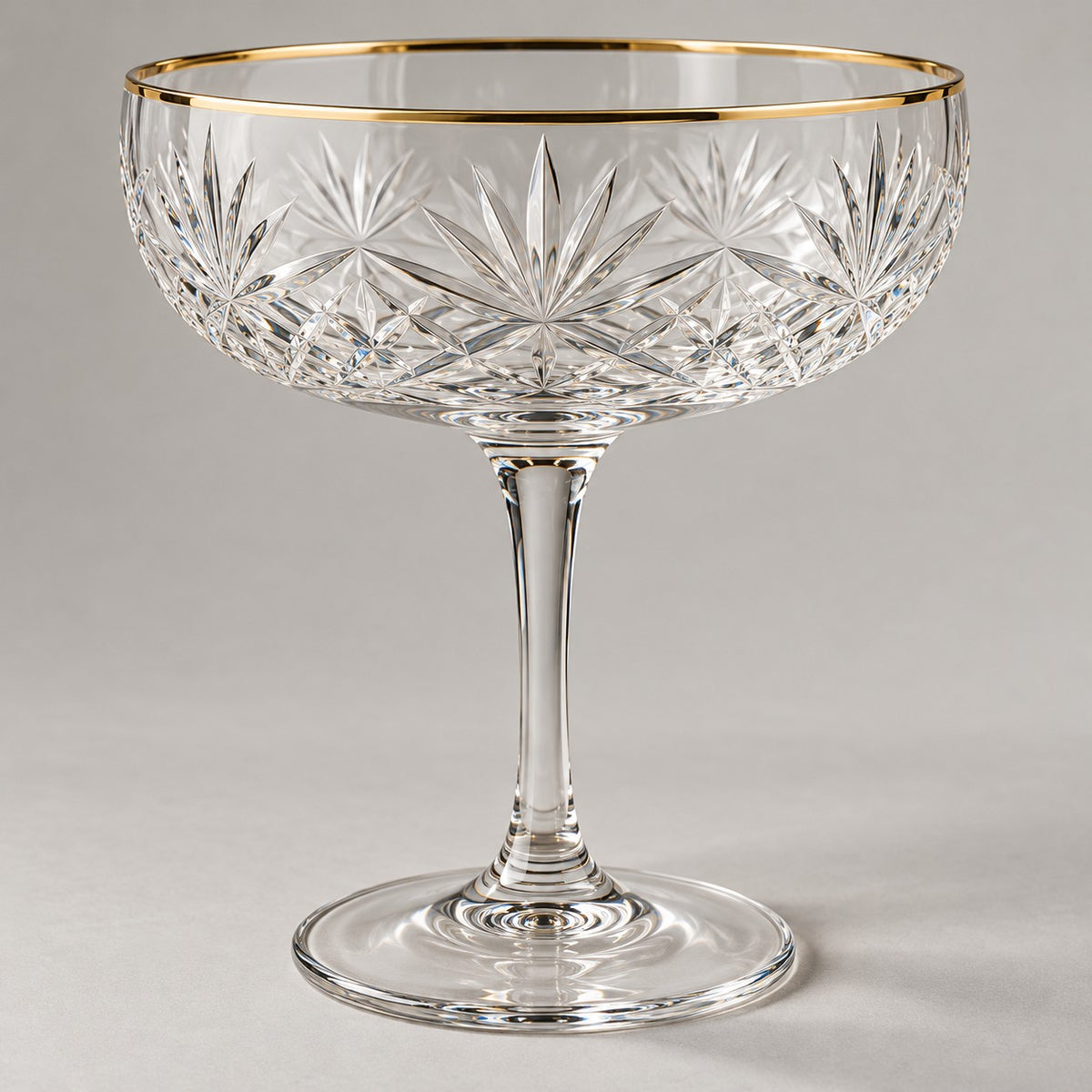 The coupe cocktail glass has a crisp engraved starburst bowl and a fine gold rim.