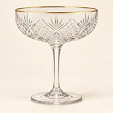 The Gold Rim coupe cocktail glass is centered on a warm ivory studio background.