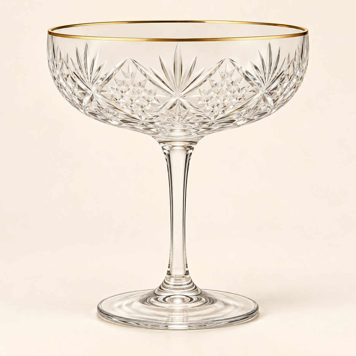 The Gold Rim coupe cocktail glass is centered on a warm ivory studio background.