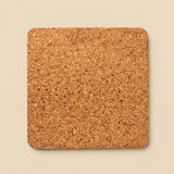 A square cork coaster with rounded corners, shown from a top-down view on a solid beige background.