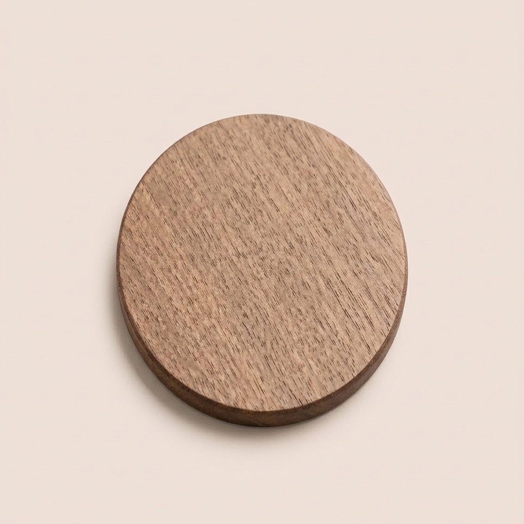 A round wooden coaster with a visible natural wood grain texture, shown from a top-down perspective on a solid, warm off-white background.