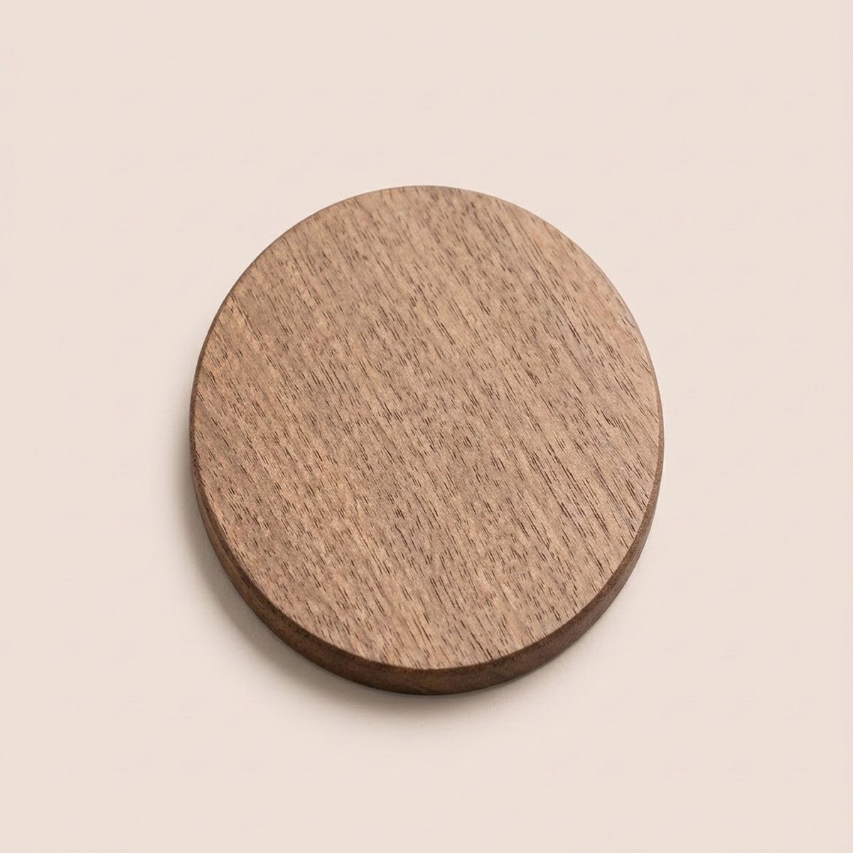 A round wooden coaster with a visible natural wood grain texture, shown from a top-down perspective on a solid, warm off-white background.
