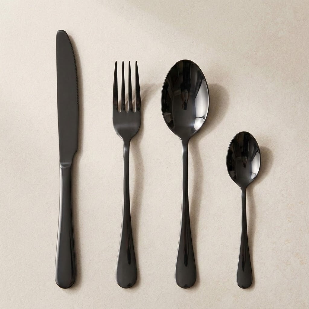 A glossy black knife, fork, tablespoon and teaspoon lie side by side on a cream background.