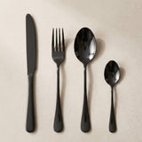 A glossy black knife, fork, tablespoon and teaspoon lie side by side on a cream background.