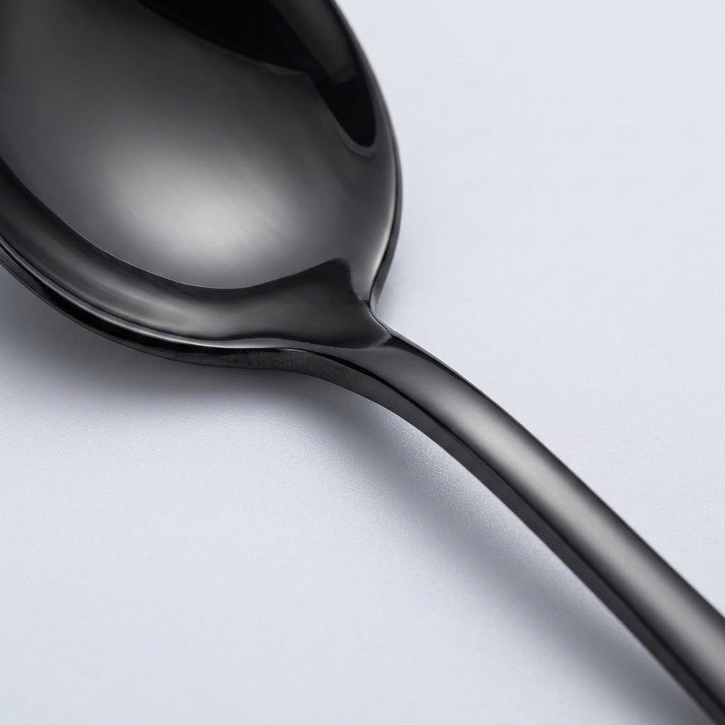 Close-up of a glossy black spoon showing its curved bowl and smooth handle against a pale grey background.