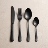 A matte black knife, fork, tablespoon and teaspoon are arranged side by side on a light beige surface.