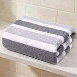 A folded plush towel with dark gray, light gray, and white stripes rests on a white shelf against cream tiles.