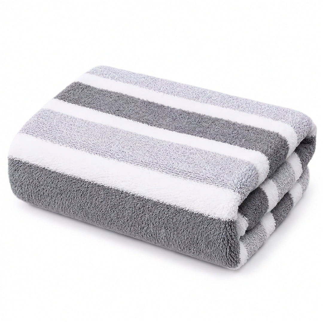 A folded plush towel with alternating dark gray, light gray, and white stripes sits against a plain white background.